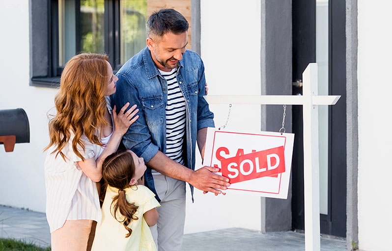 Mother, father and daughter with a SOLD sign in front of their new home